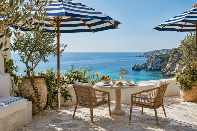 Concept imagery of a boutique hotel terrace with striped parasols overlooking the sea
